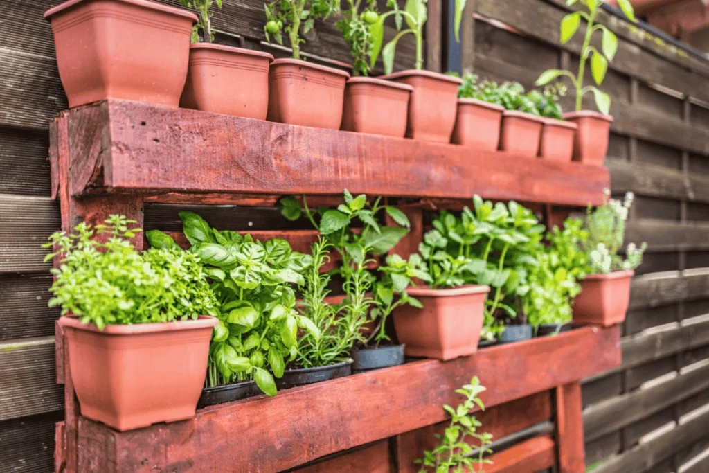 Organic vertical garden made with reused wooden pallets and clay pots, featuring a variety of fresh herbs and leafy greens for a sustainable and space-saving gardening solution.