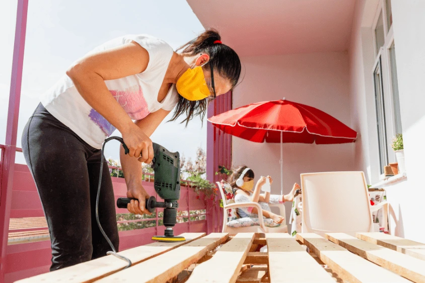Image of a person sanding or applying sealant to a wooden pallet, preparing the structure for assembling a DIY vertical garden.